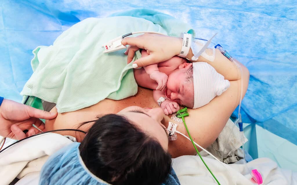Mother holding her newborn skin-to-skin after a cesarean birth in the operating room.